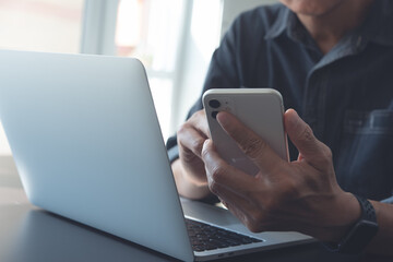 Business man using mobile phone and working on laptop computer from home office, close up
