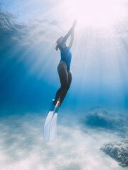 Naklejka premium Female freediver with fins glide underwater in sea with sunlight. Summer freediving.