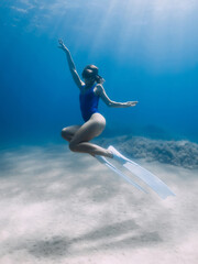 Lady freediver with fins posing and glides underwater in sea with sunlight. Freediving in warm water