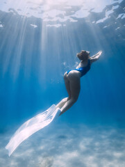Fototapeta na wymiar Attractive freediver with fins posing underwater in sea with sunlight. Slim girl underwater.
