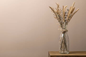 Home decor. Dried flowers is on a wooden shelf on the background of a beige wall. Copy space