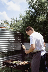 Young man grilling kebabs on skewers, man grilling meat outdoors