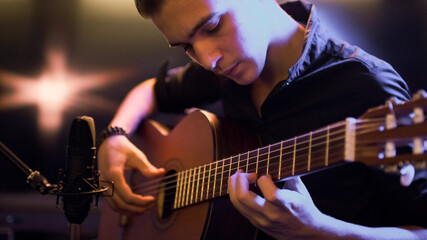 Man plays guitar. Young man plays a musical instrument. Musician records his composition in a music...
