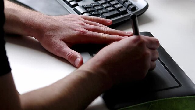 Male hands using a graphic tablet in home office as freelancer or designer for sketching and drawing with ergonomic keyboard shows inspiration and modern multimedia equipment at workplace and desktop