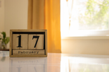 Wooden blocks of the calendar represents the date 17 and the month of February on the background of a window, curtain and a plant