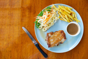 Chicken steak with vegetables salad and french fries in blue dish on wooden table.