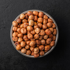 Peeled hazelnuts in a bowl on a black textured background, top view.