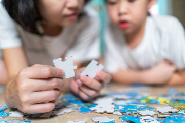 Mother holding a piece of jigsaw puzzle and teach her son to put it together with other part. Happy family at the weekend. Woman teach  child to solve problem. Relation and parent concept..