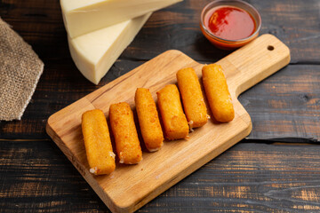 Breaded mozzarella cheese sticks with ketchup sauce on wooden cutting board