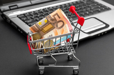 Shopping cart with euro and laptop on black background. Online shopping.