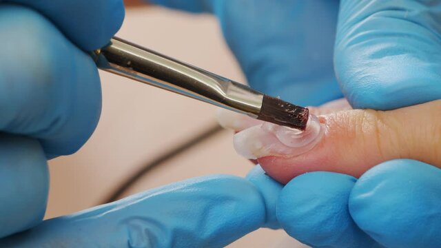 Manicurist paints nails with  gel polish. Application of acrylic polish on nails.   Application Shellac on nails.  Manicure service.  Specialist covers the nail of client by clear gel. Close up.