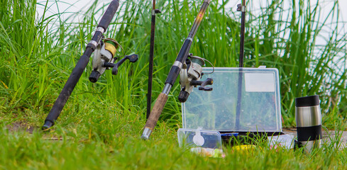 Fishing rod, spinning reel and a cup of hot coffee on the bank of the river pier. Out-of-town vacation concept. Selective focus