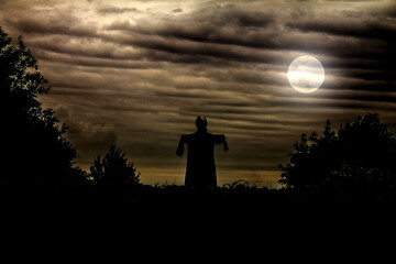 scarecrow in the garden against the full moon of a cloudy gloomy sky