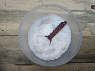 salt in a plastic container on a wooden table with selective focus