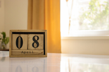 Wooden blocks of the calendar represents the date 8 and the month of April on the background of a window, curtain and a plant.
