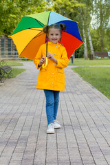 a blonde girl with ponytails in a yellow jacket and a colored umbrella plays in the park spring summer autumn