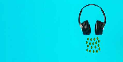 Black headphones and a green leaves on a pastel blue background. Music Abstract 3D Minimal Ad Idea.