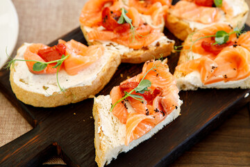 A red fish sandwich decorated with fresh herbs on a brown wooden board.