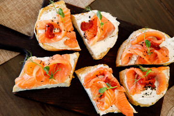 A red fish sandwich decorated with fresh herbs on a brown wooden board.