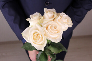 White roses in the hands of a man in a blue suit