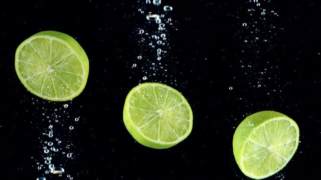Limes splashing into the water in slow motion. Three half of limes falling slowly on a black background. Organic green citrus isolated on black background. Fresh water with fruits.