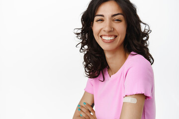 Smiling healthy woman laughing, showing shoulder with medical plaster, got vaccinated from...
