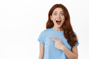 Awesome discounts. Amazed redhead girl gasp and say wow, checking out promo logo, pointing finger...