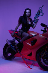 Fototapeta na wymiar Urban woman biker with rifle and sword posing on motorcycle