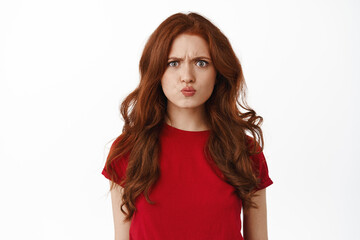 Confused and angry redhead girl pouting, frowning and grimacing, looking upset, sulking offended, being insulted or displeased, standing against white background