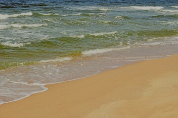 Simple beach landscape of clean golden sand and green and blue ocean with small waves breaking on the shore, no people