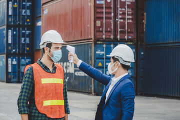 factory worker man body temperature checking fever by digital thermometer on engineer man with cargo container in background at container cargo harbor, industrial, logistic import and export concept