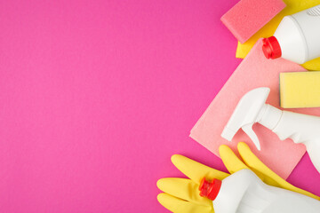 Top view photo of pink and yellow viscose rags rubber gloves sponges white detergent bottles on isolated pink background with blank space on the left