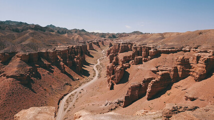 Fototapeta premium Grand canyon Charyn. Rocks from sedimentary rocks. Huge cracks in the rocks. The ground is red-orange. Top view from a drone. There is a road in the center. Layers of earth in different colors.