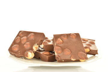 Several slices of dark chocolate with nuts on a white ceramic saucer, close-up, isolated on white.