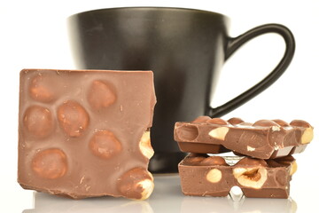 Several slices of dark chocolate with nuts in a ceramic cup, close-up, isolated on white.