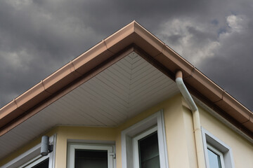 brown metal rain gutter on house roof and dark sky. concept : preparing maintenance rain gutter before rainy season.