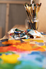 Fototapeta premium Painting palette and paint brush in glass jar on wooden table or windowsill. Art still life