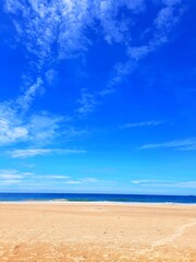 Krajobraz plaży z niebieskim niebem i chmurami oraz żółtym piaskiem.