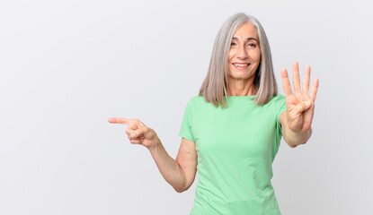 middle age white hair woman smiling and looking friendly, showing number four and pointing to the side