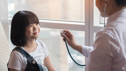 Pediatric care with happy child patient and pediatrician doctor examining Asian girl kid heart and lung health with stethoscope in medical clinic, healthcare checkup service concept