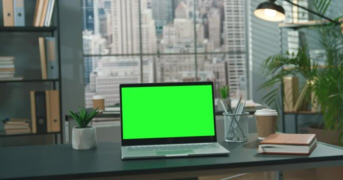 Full length view of the laptop with green blank mockup screen is on top of wood table with modern office at the background. Technologies concept