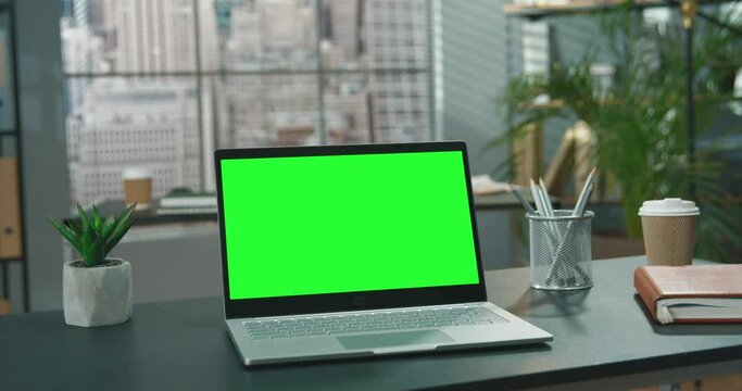 Personal computer with mock-up green screen monitor standing on the office desk with empty modern office in the background at the daytime. Business concept