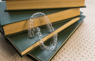 plastic dental aligners near stack of books with green cover on gray background