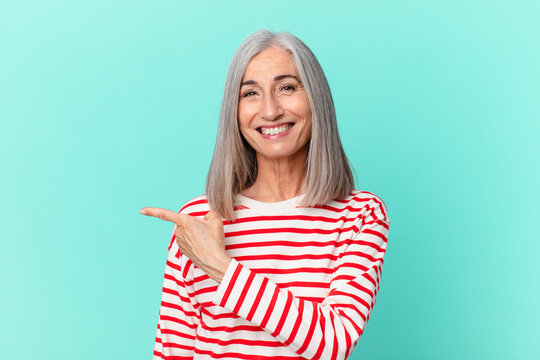 middle age white hair woman smiling cheerfully, feeling happy and pointing to the side