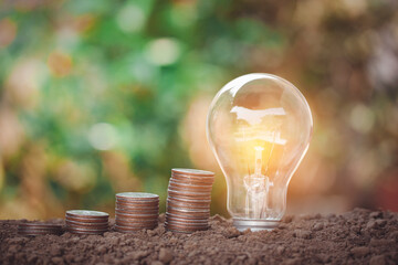 Light bulb and money stacking of coins for new concept, new idea, saving energy, saving money, thinking about financial growth up on bokeh background.