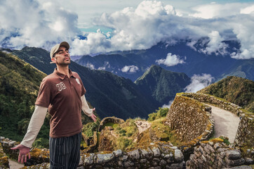 High angle view of a man breathing the air with eyes closed and open arms, with huge valley behind, on Phuyupatamarca ruins. Inca trail to Machu Picchu in Peru. South America