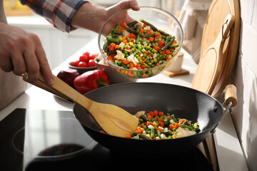 Man pouring mix of fresh vegetables into frying pan, closeup