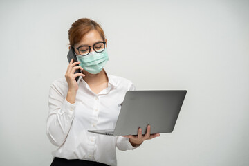 Asian female office worker wearing a mask using a laptop and talk on the mobile phone to contact the job financial transactions