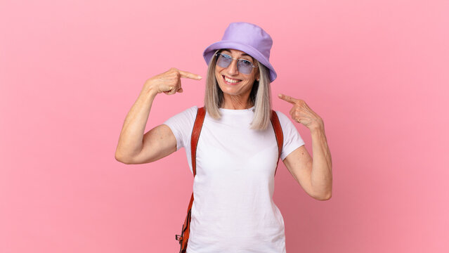 middle age white hair woman smiling confidently pointing to own broad smile. summer concept
