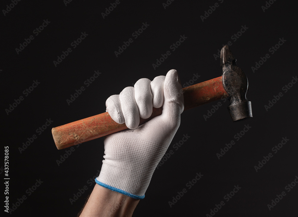 Wall mural retro hammer tool in male hand in white building gloves close up over black background.